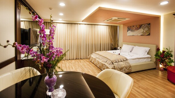 A hotel room with a bed, a dining table with chairs, a vase of flowers, and a large mirror. - Adana Erten Otel (Adana)