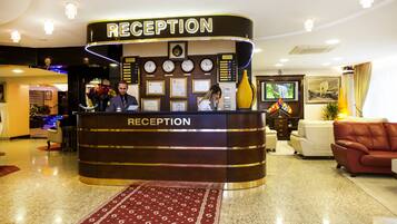 Un mostrador de recepción con un reloj, diplomas enmarcados y una pantalla digital.
