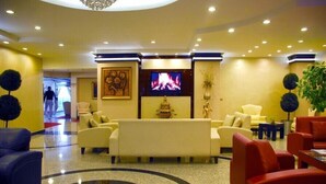 A lobby with a central seating area, a television screen, and a decorative wall piece. - Adana Erten Otel (Adana)