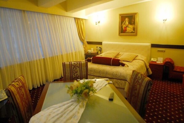A hotel room with a bed, a table with a vase of flowers, a painting on the wall, and a window with curtains.