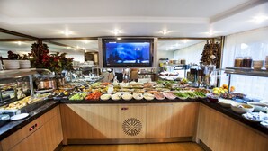 A buffet with various food items and a television screen displaying a program. - Adana Erten Otel (Adana)