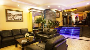 A hotel lobby with black leather sofas, a coffee table, a framed picture on the wall, and a staircase with blue lighting. - Adana Erten Otel (Adana)