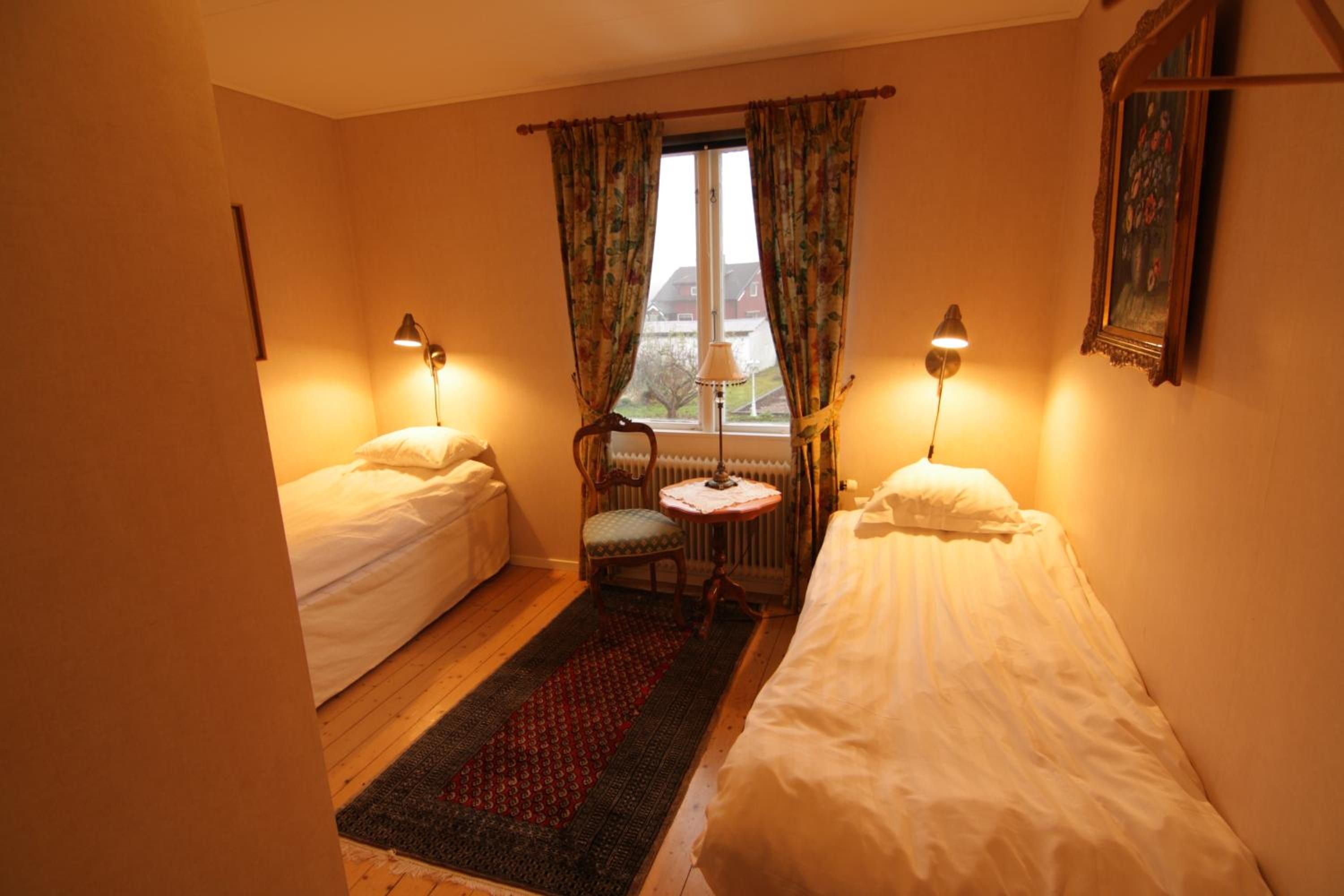Une chambre avec deux lits simples, une petite table, une chaise et une fenêtre avec des rideaux.