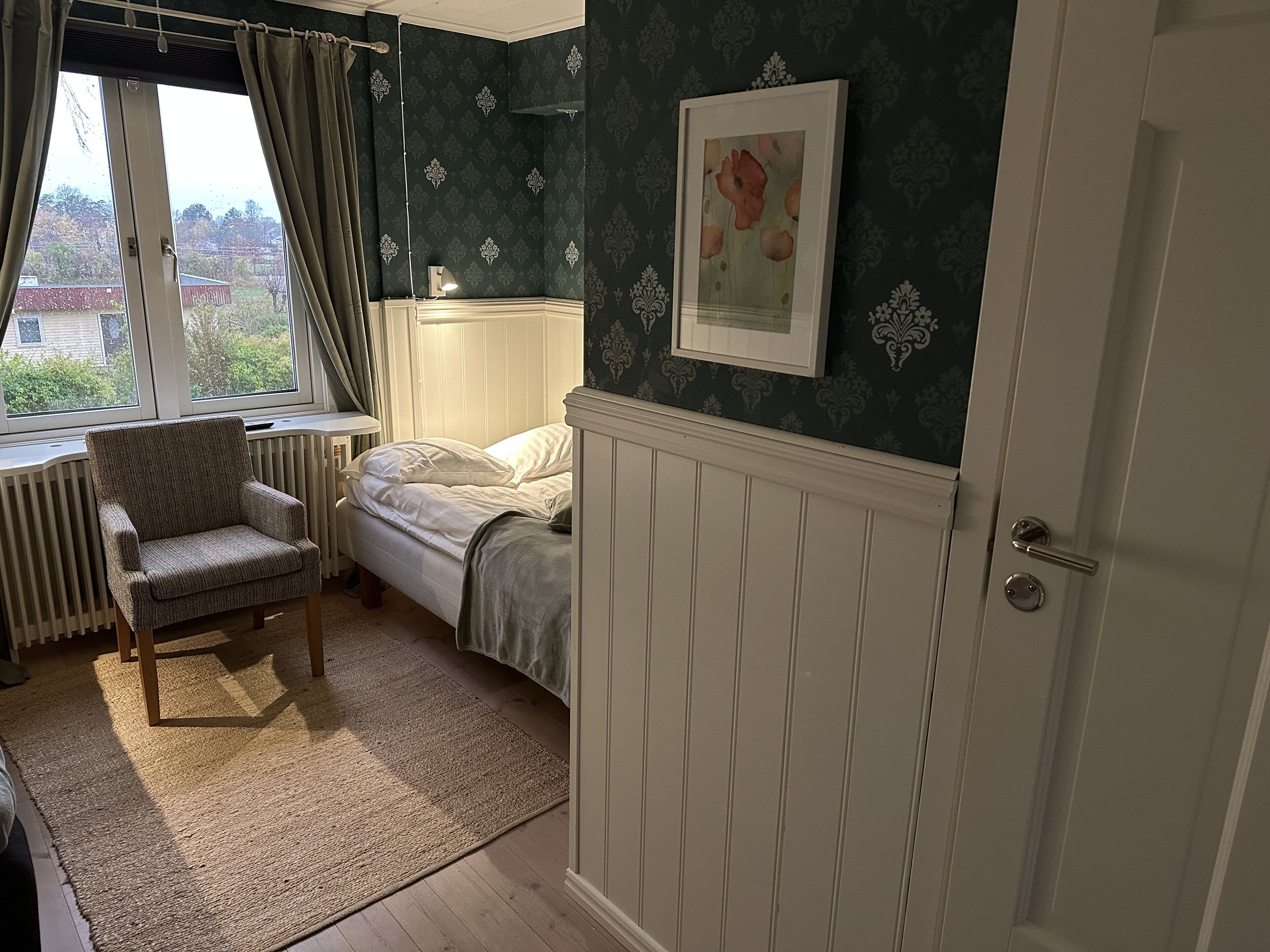 A bedroom with a bed, a chair, a radiator, and a window with curtains.