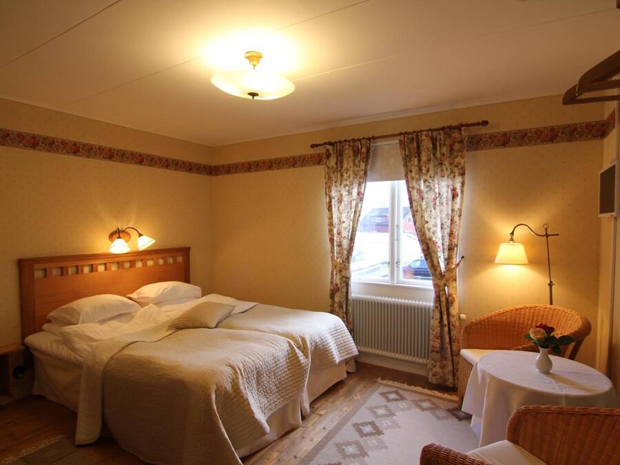 A hotel room with two beds, a small table with a vase, and a window with curtains.