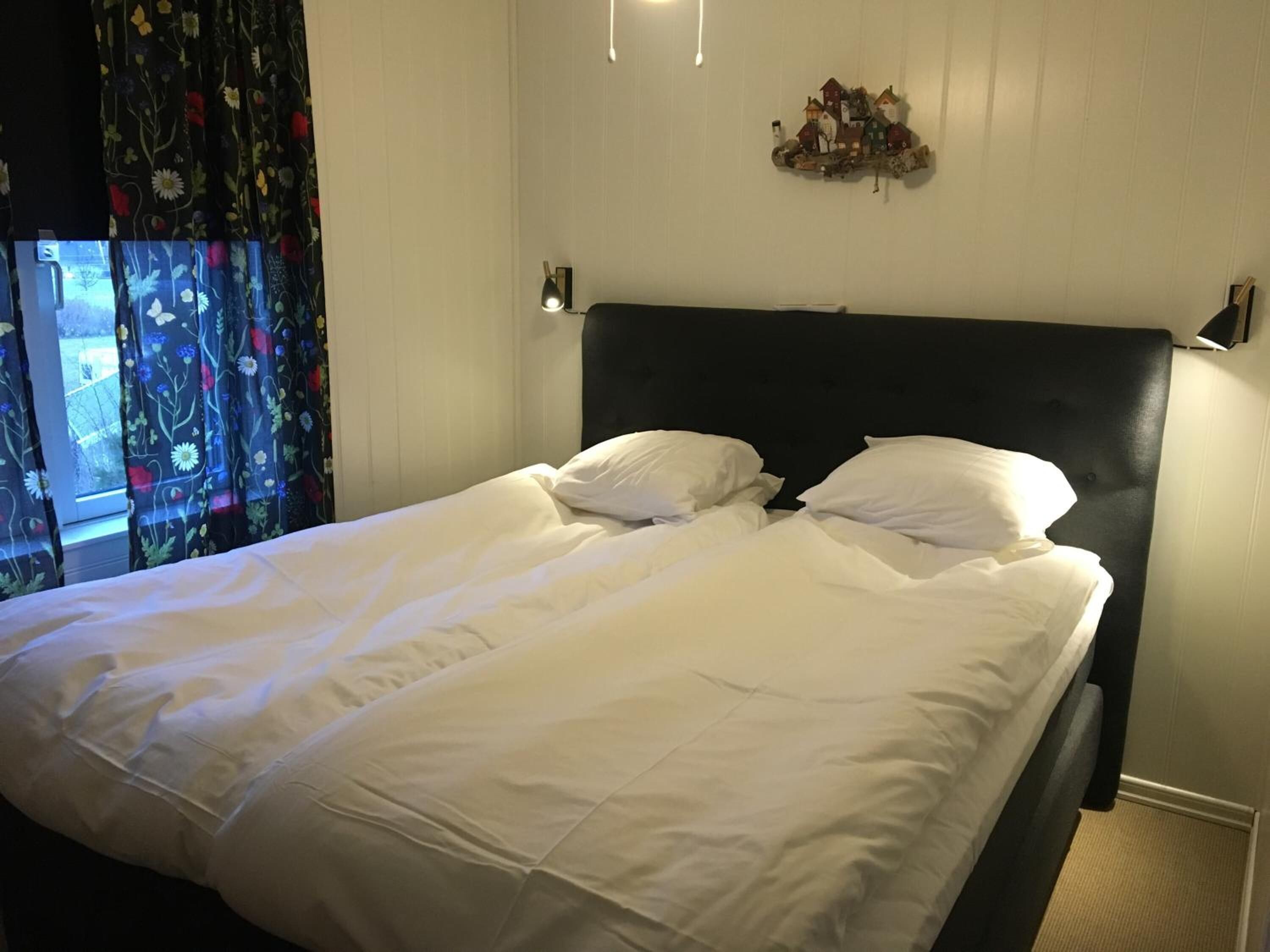 Una cama bien hecha con sábanas blancas, cabecero oscuro y un pequeño adorno encima.