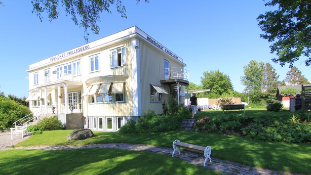 Ein großes, zweistöckiges Gebäude mit einem Balkon im zweiten Stock, einem Kiesweg, der zum Eingang führt, und einem gepflegten Rasen mit einer Bank.