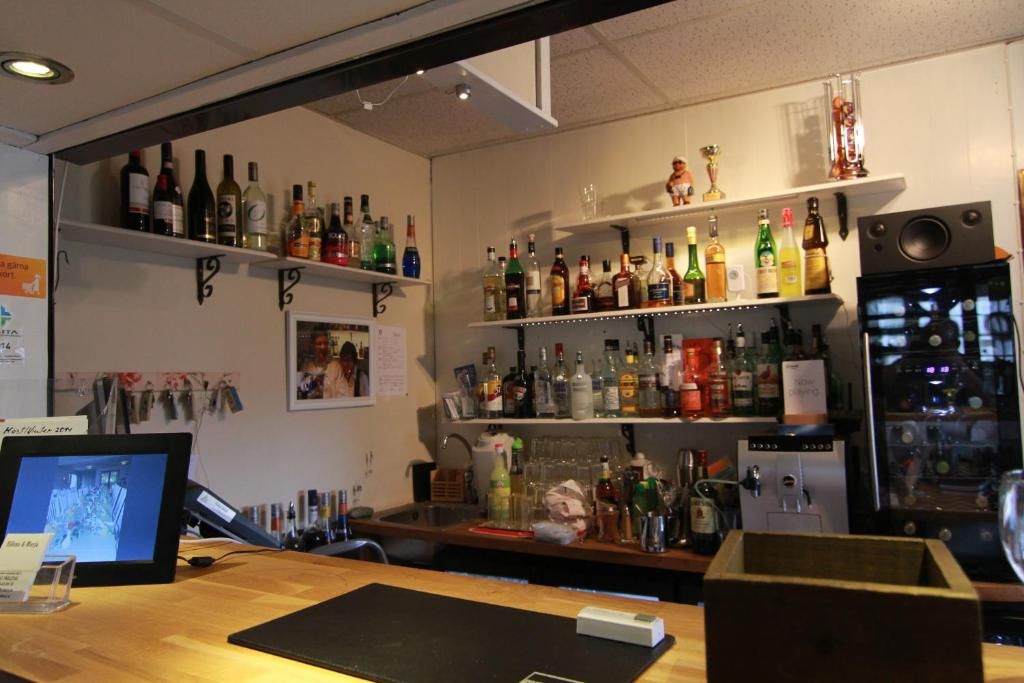 A bar area with shelves of various liquor bottles, a refrigerator, and a digital screen displaying a photo.