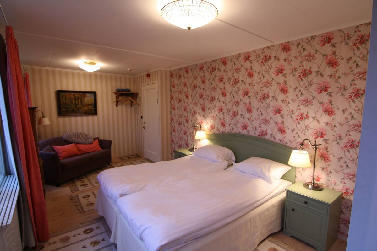 Un dormitorio con cama, mesitas de noche, cómoda, un cuadro y un papel tapiz floral.