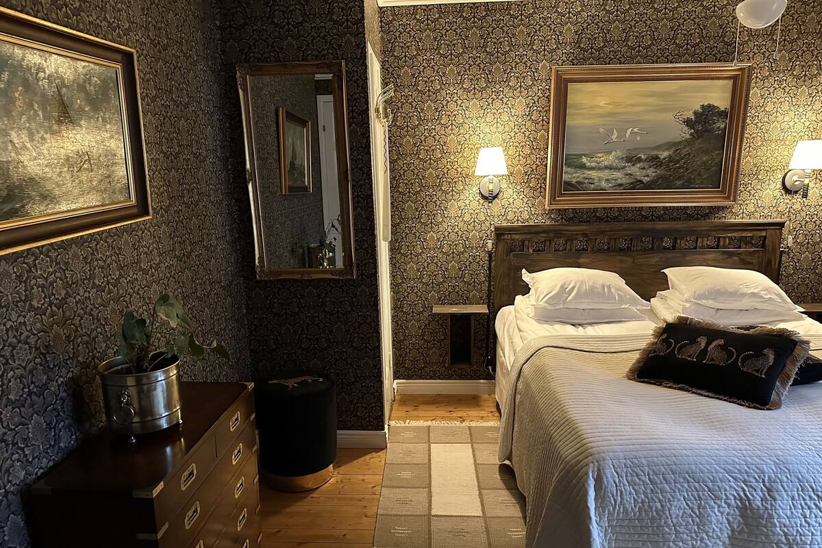 Una habitación de hotel con una cama de madera, un aparador, un espejo y dos lámparas fijadas a la pared.