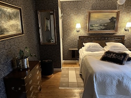 Una habitación de hotel con una cama de madera, un aparador, un espejo y dos lámparas fijadas a la pared.