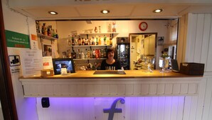 Eine Bar mit einer Theke, Regalen voller Flaschen, einem Kühlschrank und einer Wanduhr.