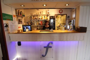 Una zona de bar con mostrador, estanterías con botellas, un refrigerador y un reloj en la pared.