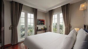 Ein Hotelzimmer mit einem großen Bett, einem an der Wand befestigten Fernseher und einem Balkon mit Vorhängen.