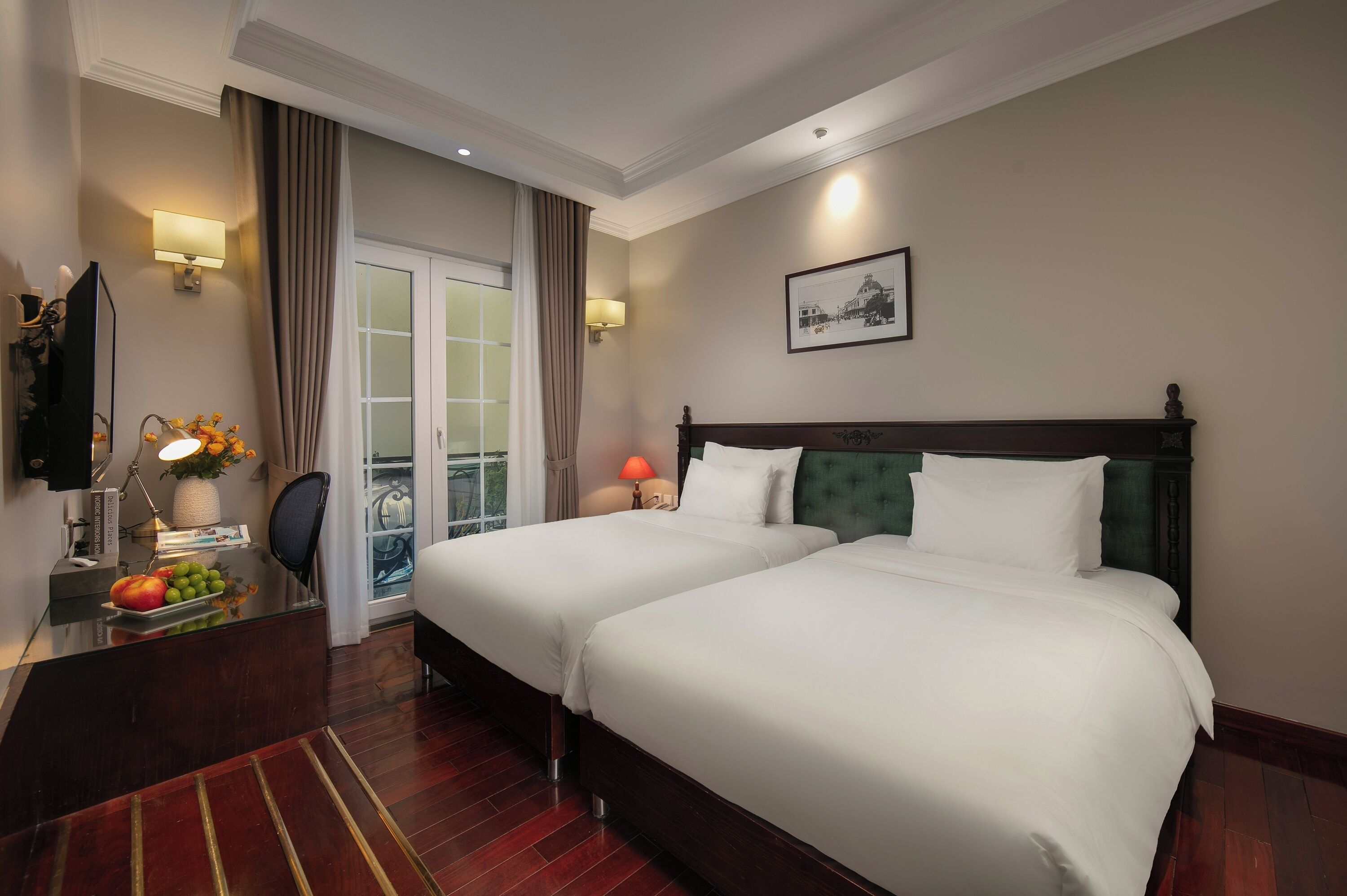 A hotel room with two beds, a desk with a lamp, a TV, and a view of the outdoors through a glass door.