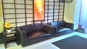 A living room with a black leather sofa, a small table with a potted plant, and a decorative wall panel. - Hotel Sogo Sta Mesa (San Juan)