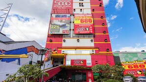 A multi-story hotel with a prominent red and yellow facade, multiple balconies, and various promotional signs advertising discounts and stay promotions. - Hotel Sogo Sta Mesa (San Juan)