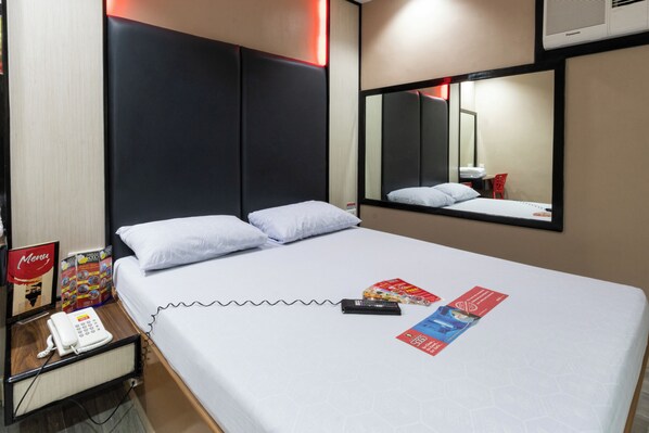 Una habitación de hotel con una cama, una mesita de noche con un teléfono, un espejo y un atril para el menú.
