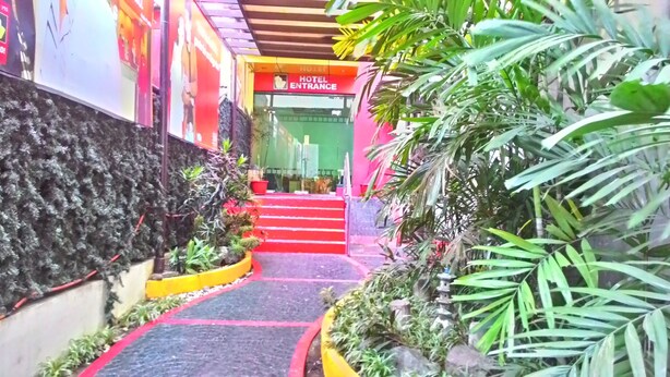 A hotel entrance with a red carpet leading up to the door, surrounded by potted plants and a stone wall. - Hotel Sogo Sta Mesa (San Juan)