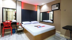 A hotel room with a large bed, a red chair, a small table, a trash bin, and a mirror. - Hotel Sogo Sta Mesa (San Juan)