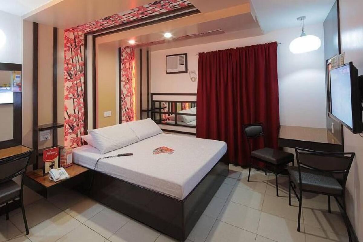 A hotel room with a bed, a desk, a chair, a TV, and a red curtain.