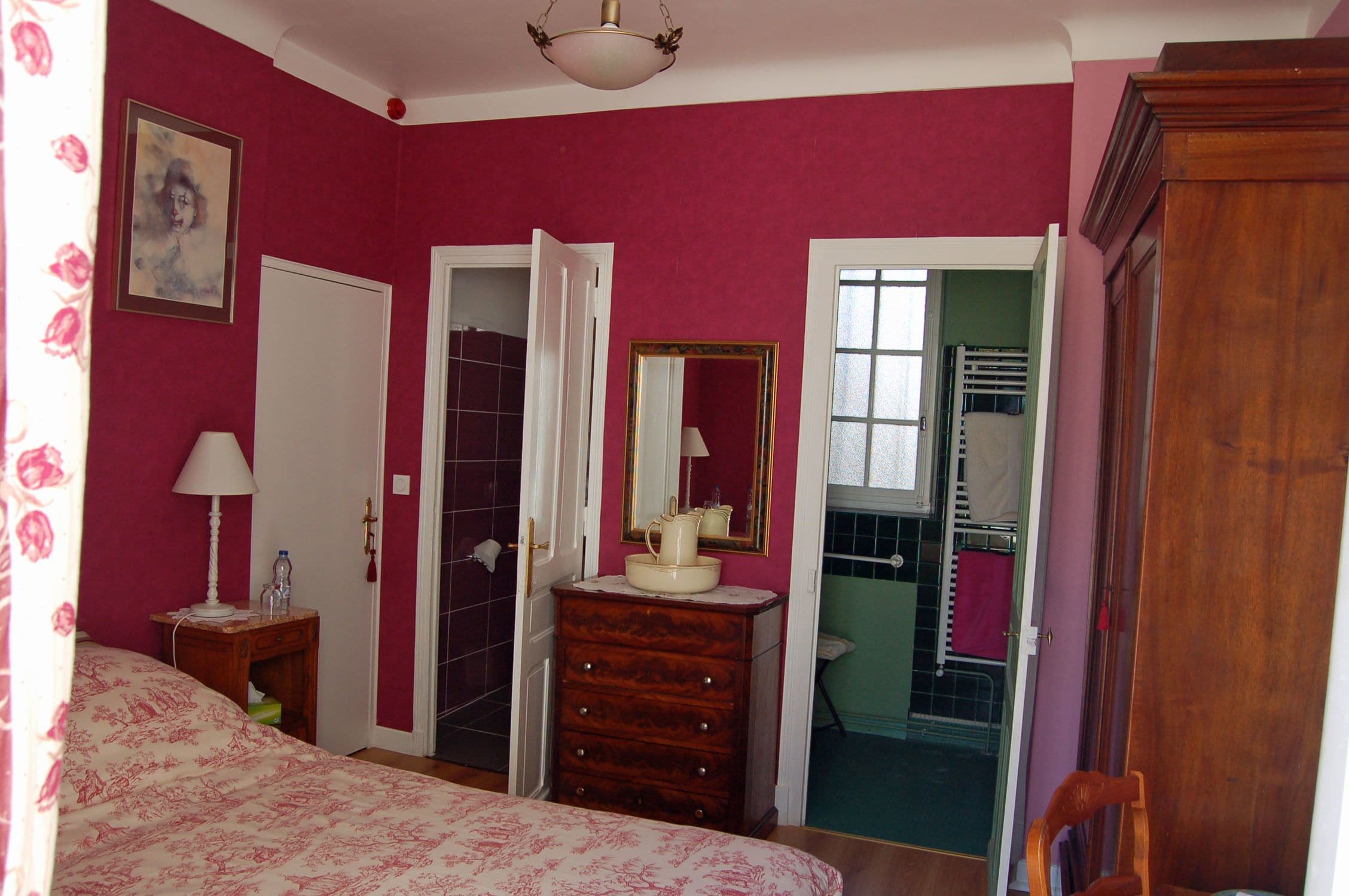 A bedroom with a bed, dresser, and a mirror. There is a door leading to a bathroom.