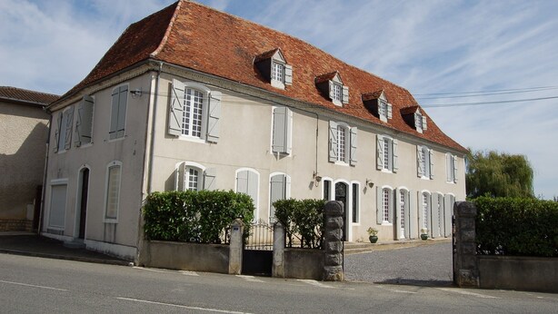 Um edifício de dois andares com fachada simétrica, várias janelas e telhado de telhas vermelhas.