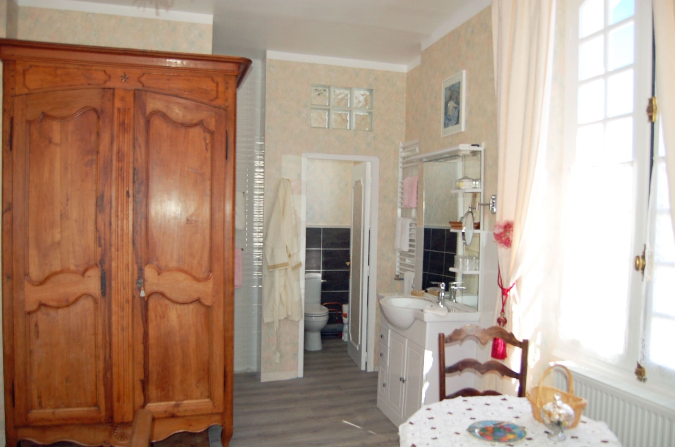 Una habitación con un armario de madera, un baño con inodoro y lavabo, y una mesa con una cesta y un plato.