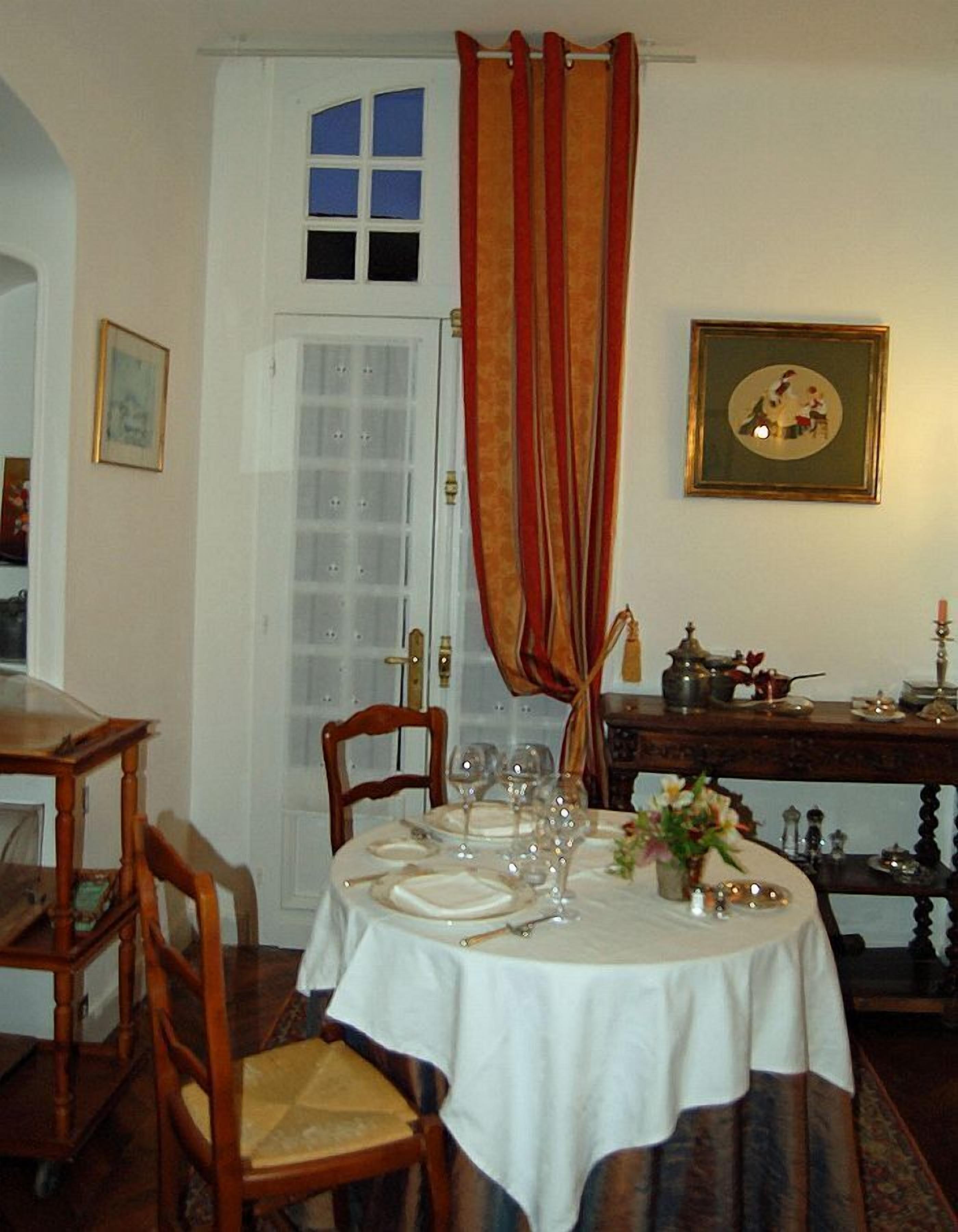 A dining room with a round table set for four, a wooden chair, a door with a window, and a wall with a framed picture.