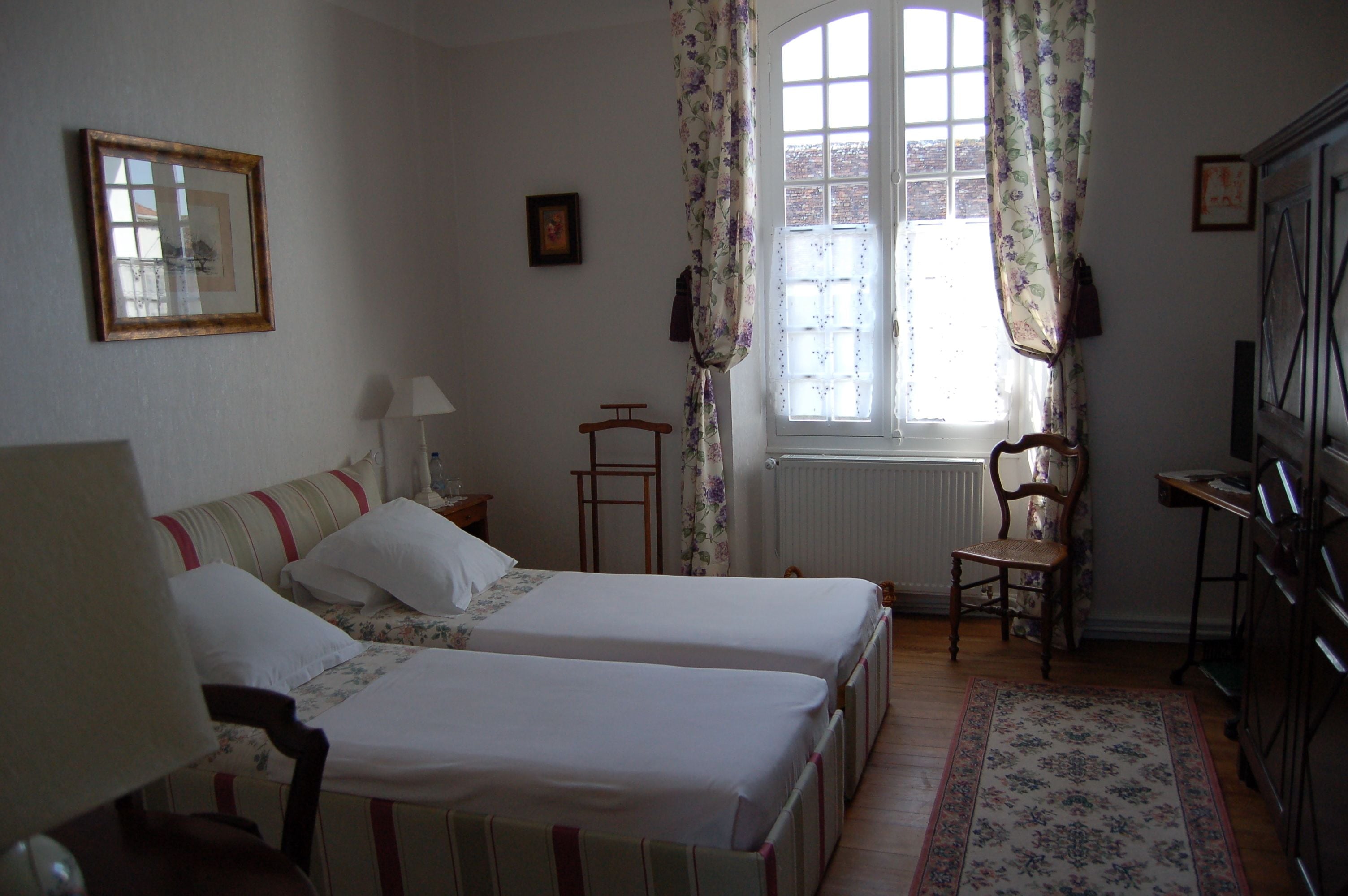 Una habitación con dos camas, una silla, una mesa y un ventanal con cortinas.