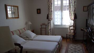 Una habitación con dos camas, una silla, una mesa y un ventanal con cortinas.
