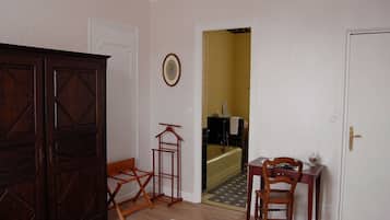 Quarto com guarda-roupa de madeira, uma cadeira pequena de madeira, uma mesa com cadeira e uma porta que dá para o banheiro.