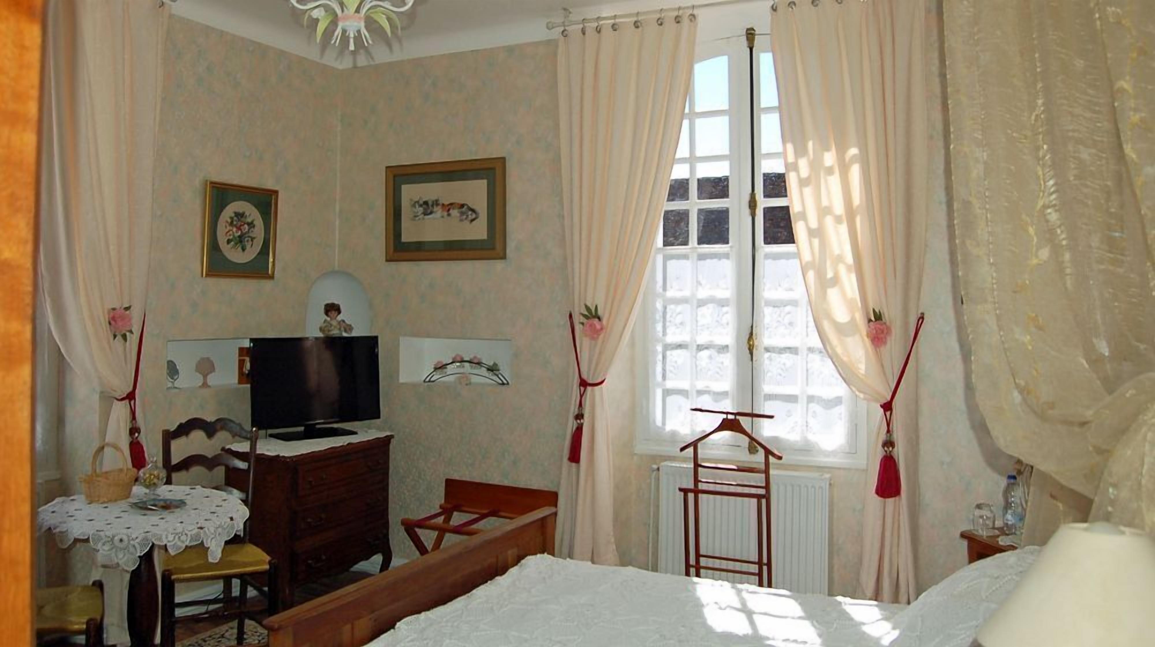 Quarto com cama, penteadeira, televisão e janela com cortinas.