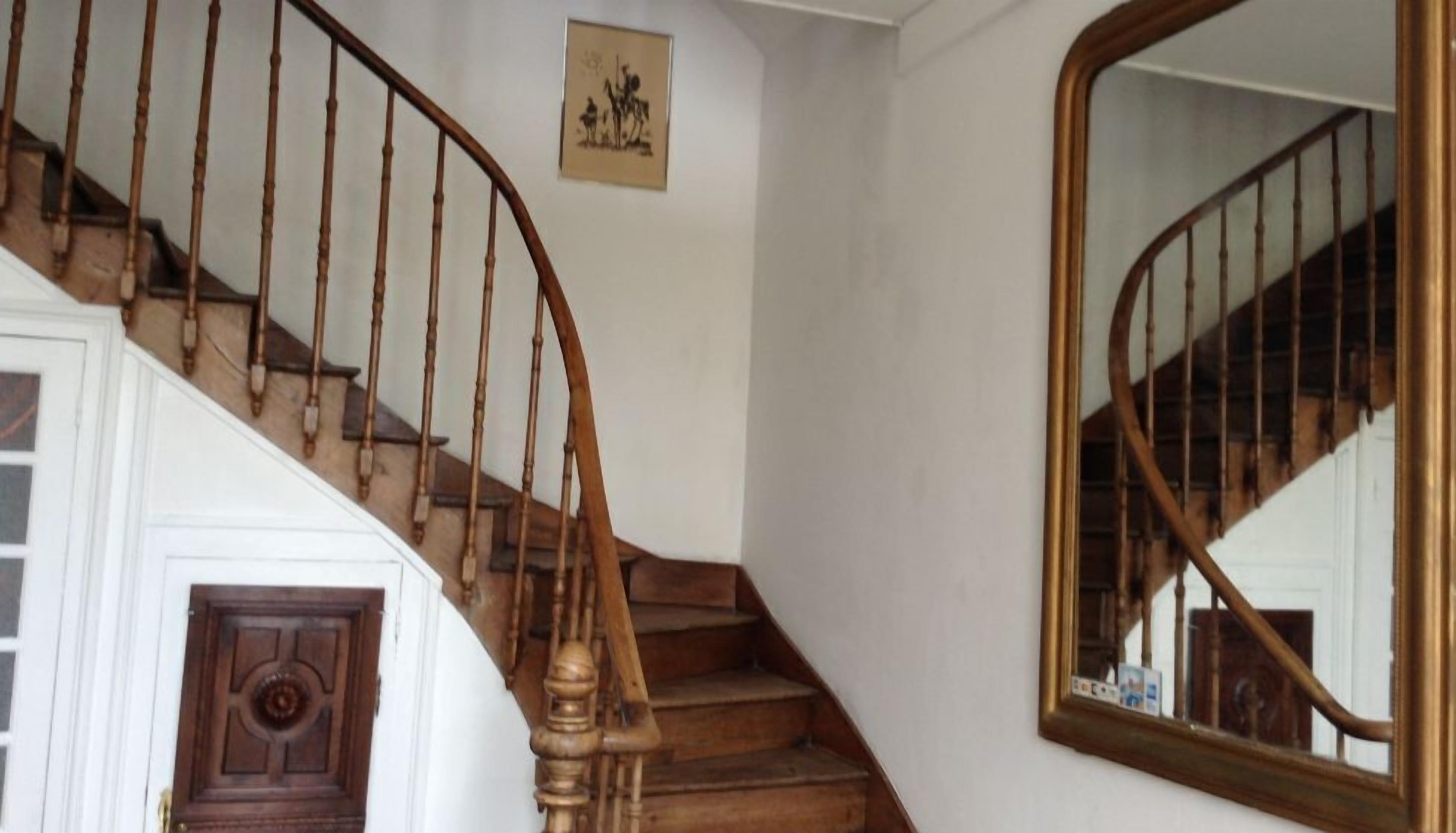 A wooden staircase with a curved design, a wall-mounted mirror, and a framed picture.
