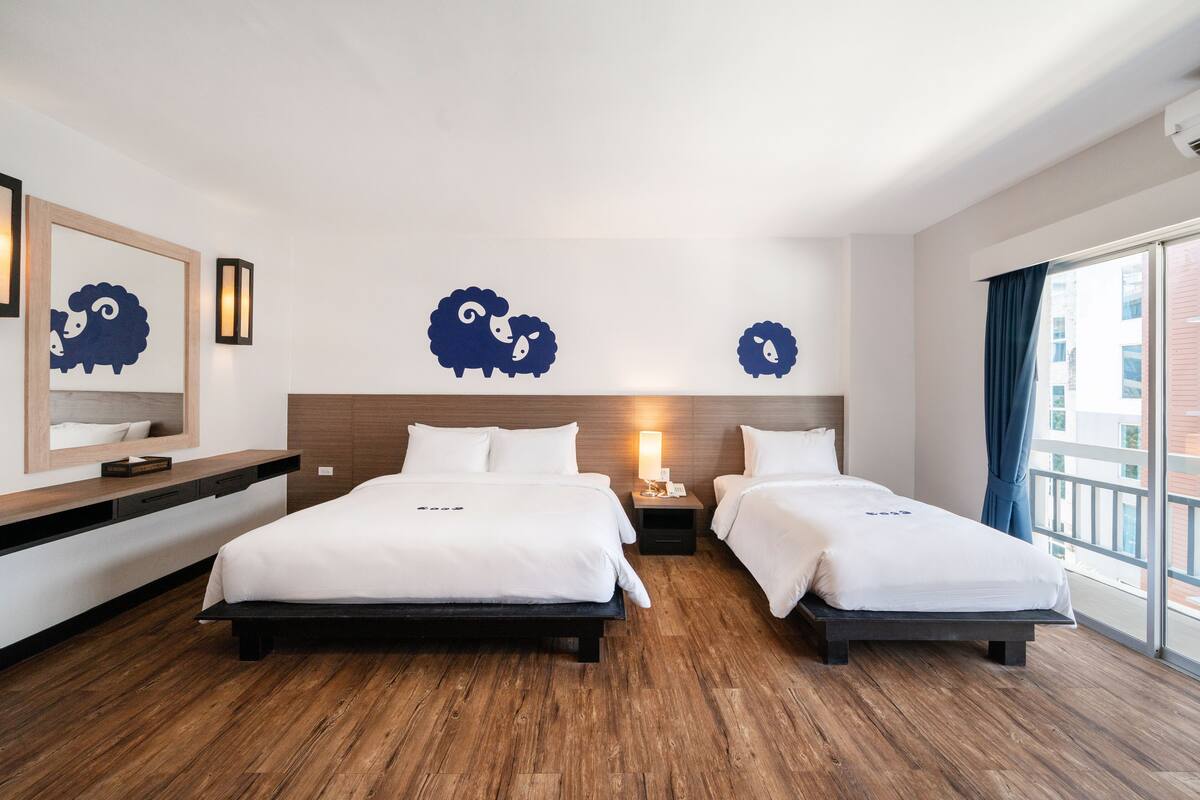 A hotel room with two beds, a wooden floor, a large window with a view, and wall art.
