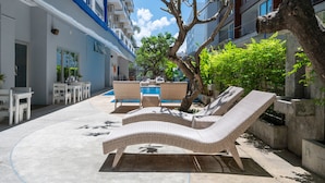 Un espace aménagé au bord de la piscine, avec des chaises longues, une piscine et un bâtiment doté de balcons.