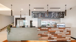 Un café moderne avec un comptoir à l’aspect pierre, un tableau affichant le menu au-dessus, et un escalier menant à un autre niveau.