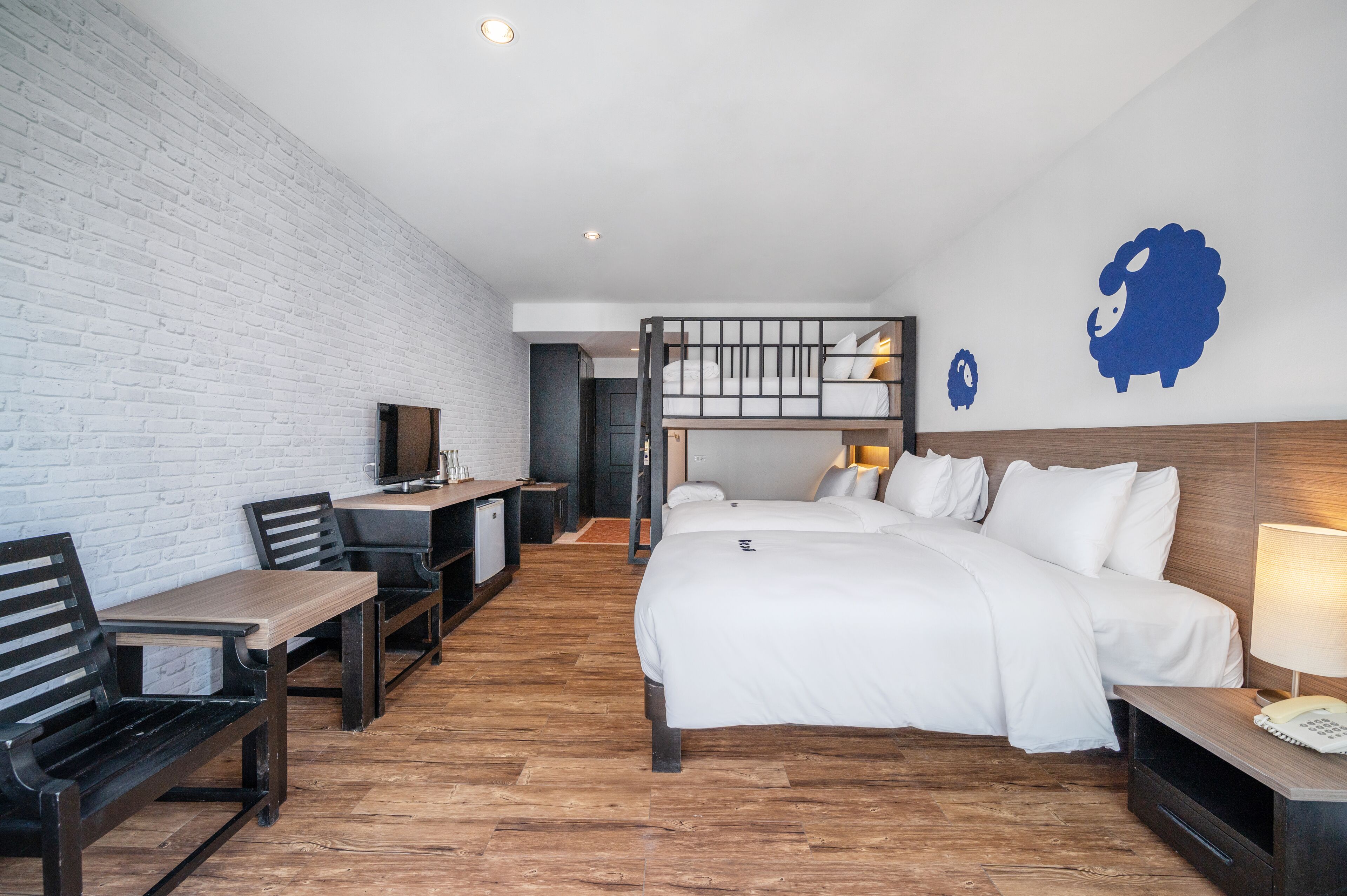 Habitación de hotel con literas, un escritorio con silla, una pequeña kitchenette y un televisor.