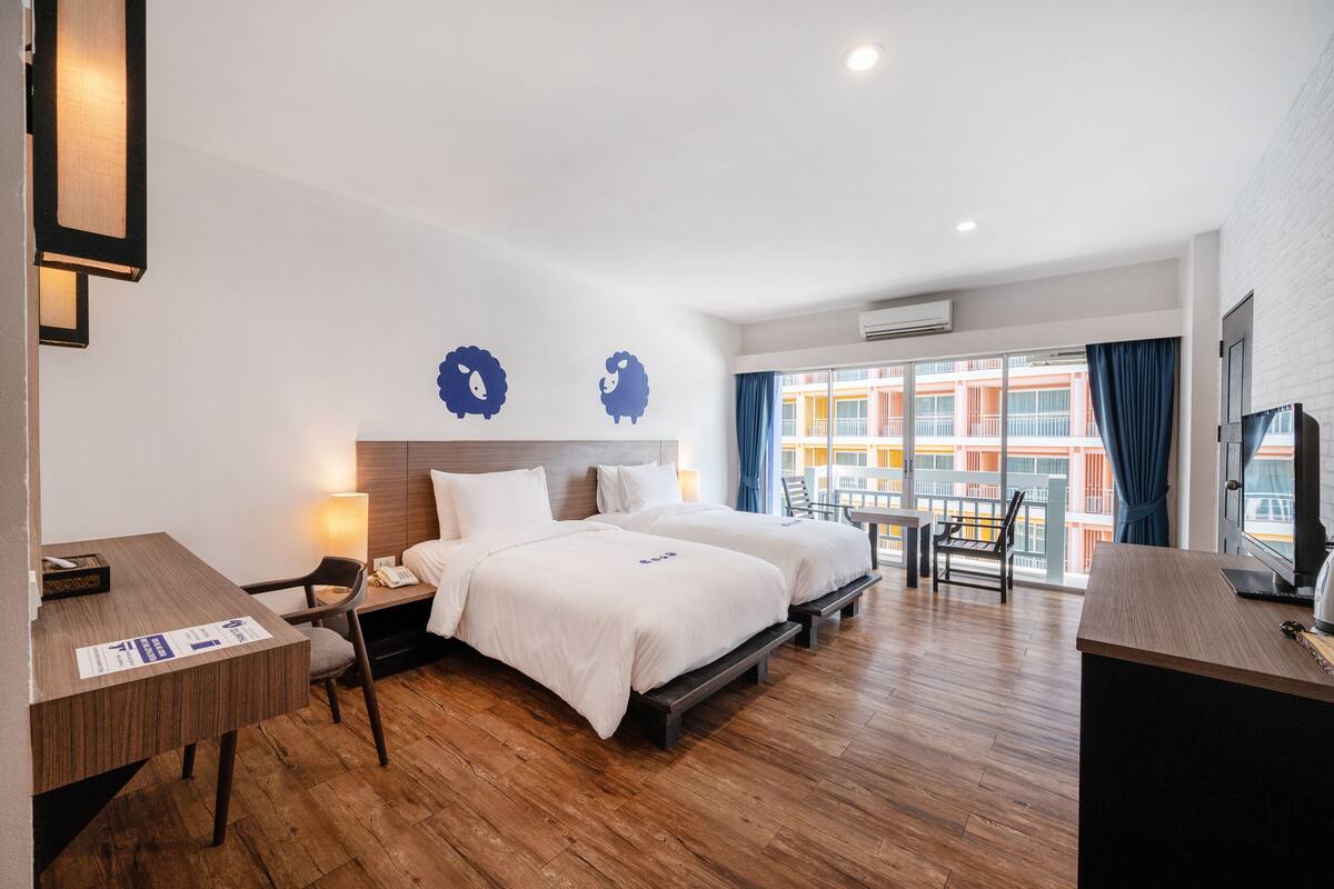 A hotel room with two beds, a desk, a chair, and a TV.