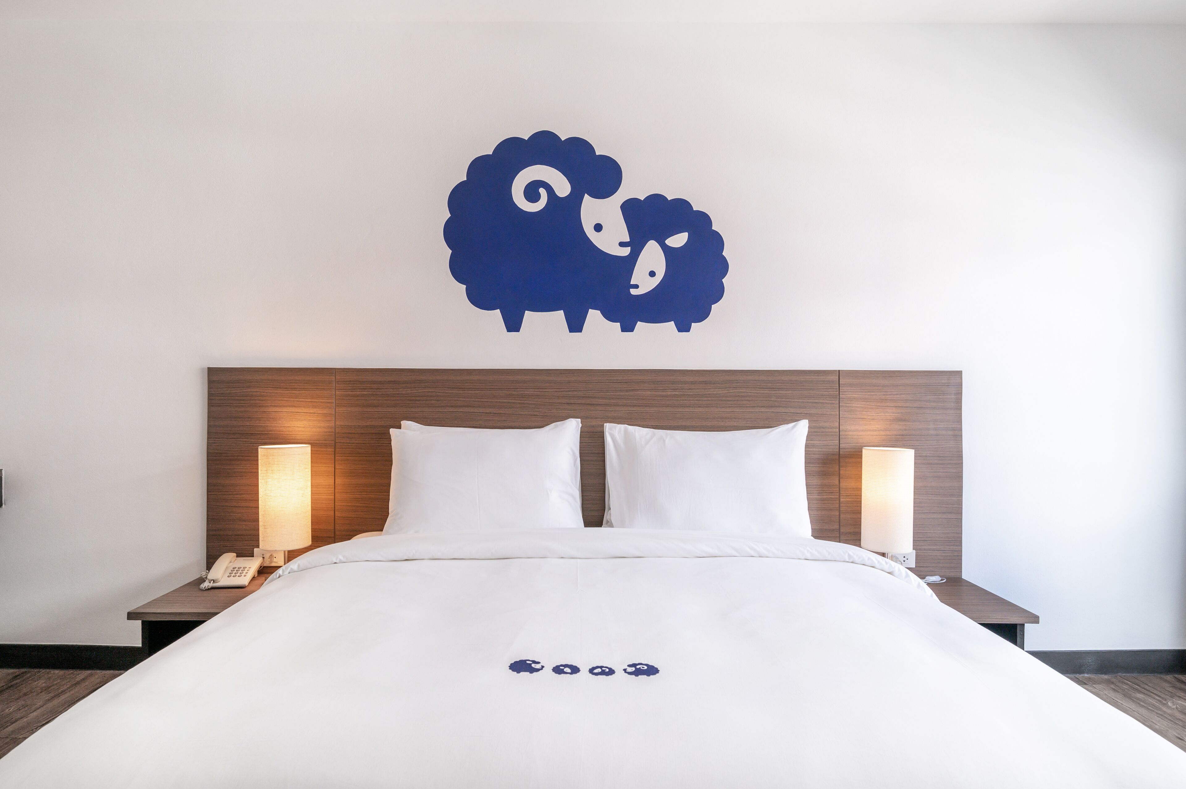 Una cama bien hecha con ropa de cama blanca, un cabecero de madera y una obra de arte en la pared con una oveja.