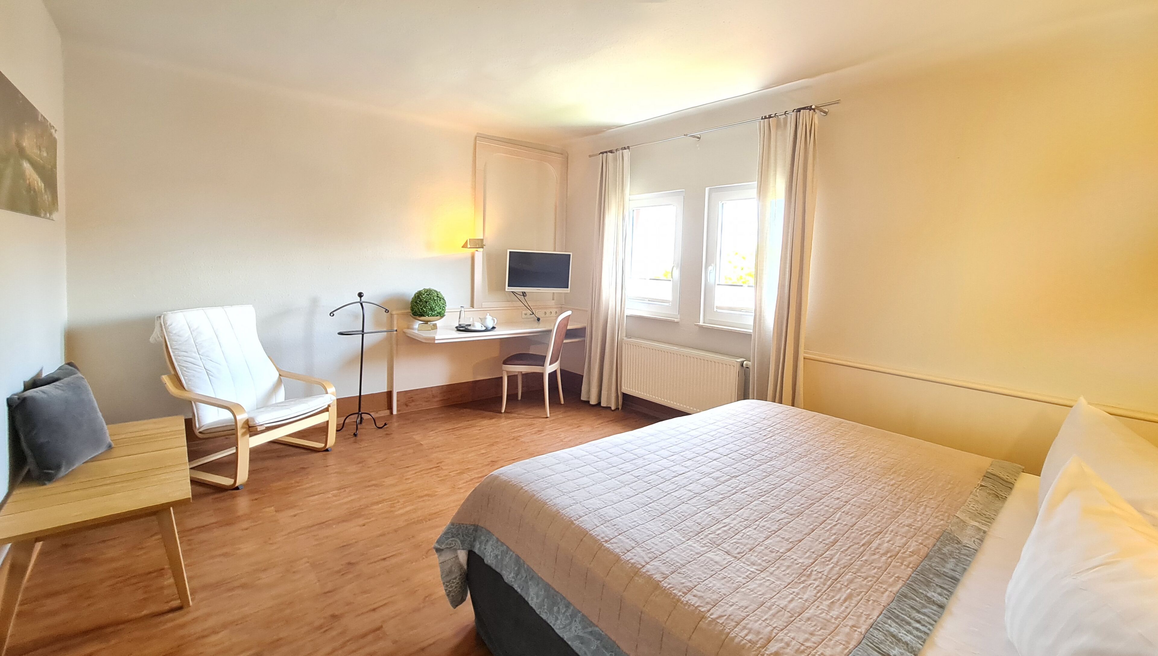A hotel room with a bed, a desk with a computer, a chair, and a window with curtains.