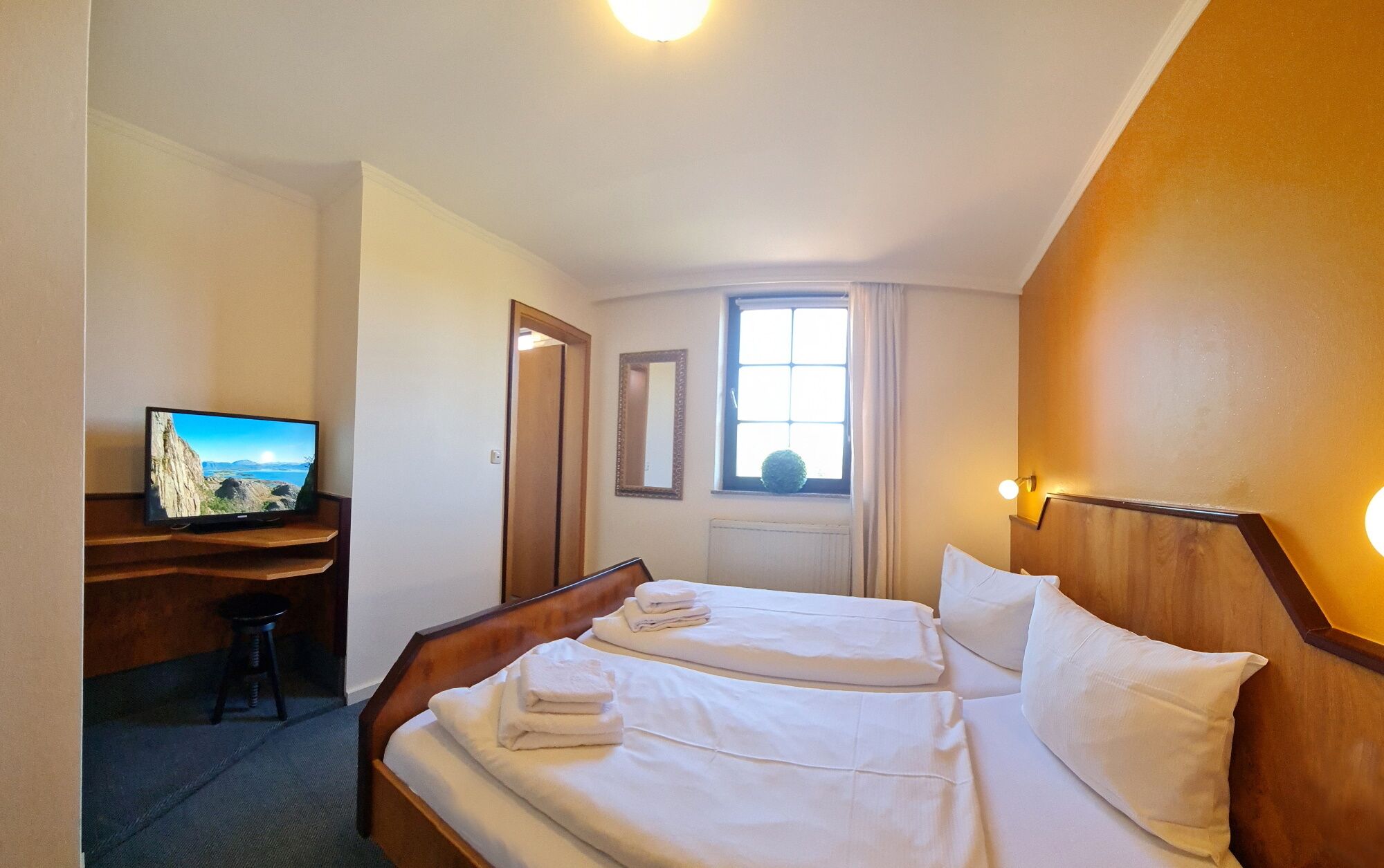 Una habitación de hotel con una cama, un escritorio con televisor, un espejo y una ventana.