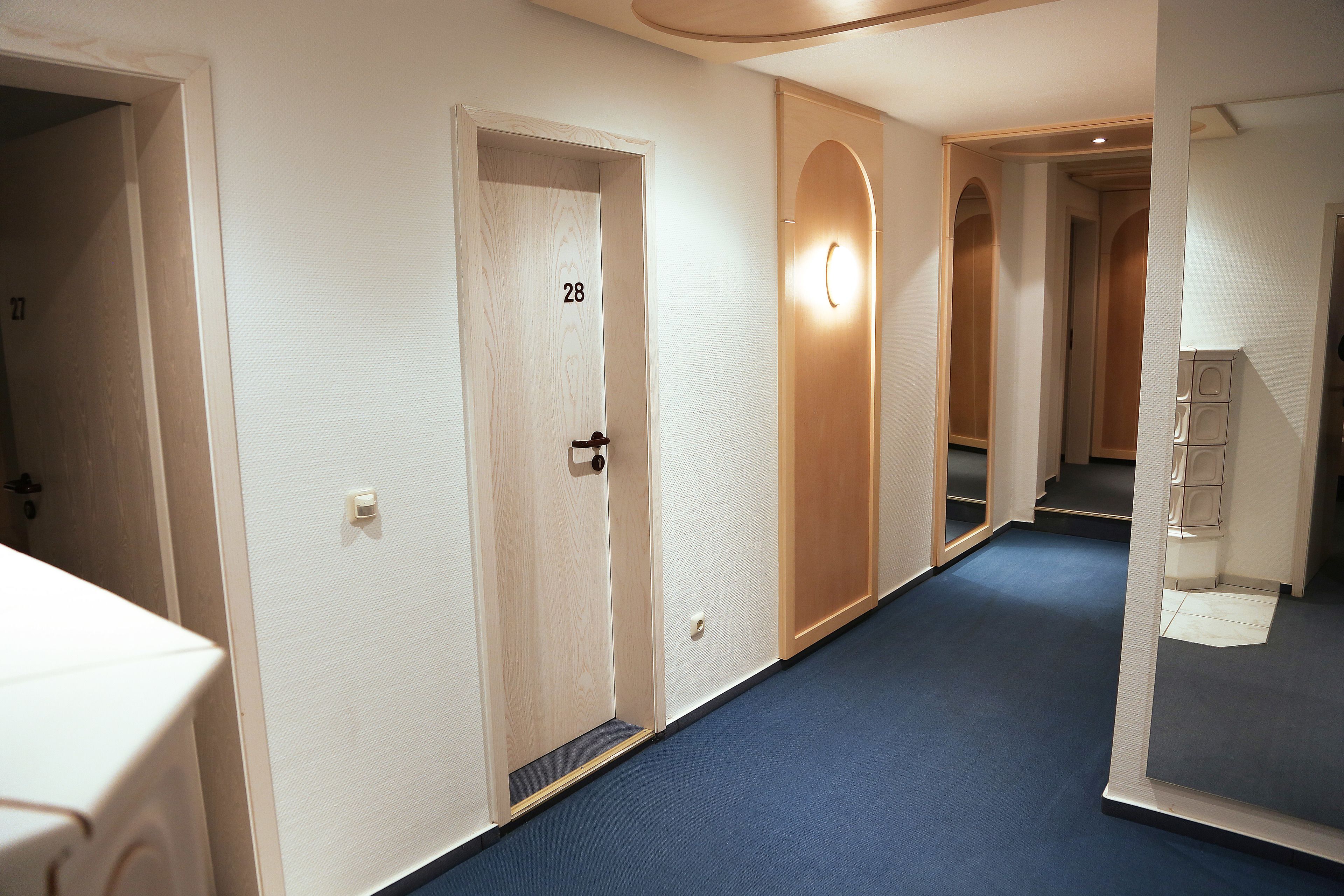 A hallway with doors numbered 28 and 29, wooden doors, and a blue carpeted floor.