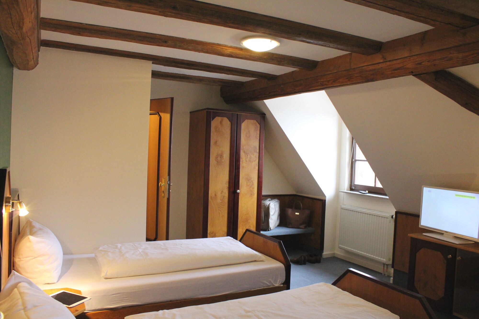 Een slaapkamer met twee bedden, houten balken, een kledingkast, een televisie en een raam.
