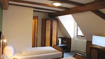 Een slaapkamer met twee bedden, houten balken, een kledingkast, een televisie en een raam.