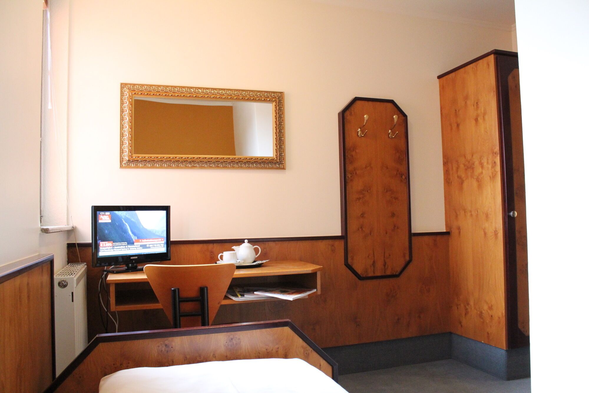 Una camera d'albergo con un letto, una scrivania con un computer, una sedia, uno specchio e un armadio.
