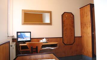 Una camera d'albergo con un letto, una scrivania con un computer, una sedia, uno specchio e un armadio.