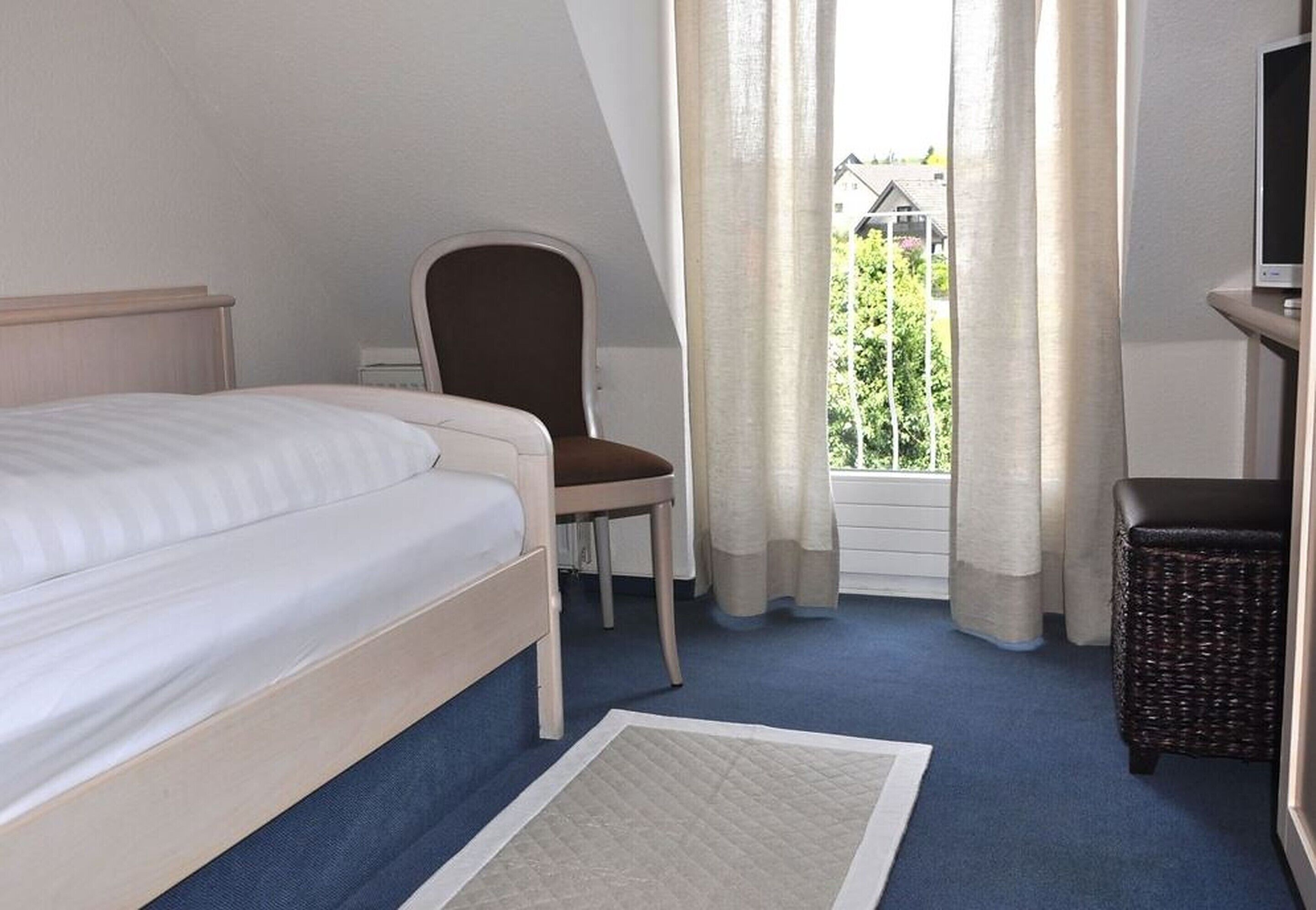 A bedroom with a bed, a chair, a small table, and a window with curtains.