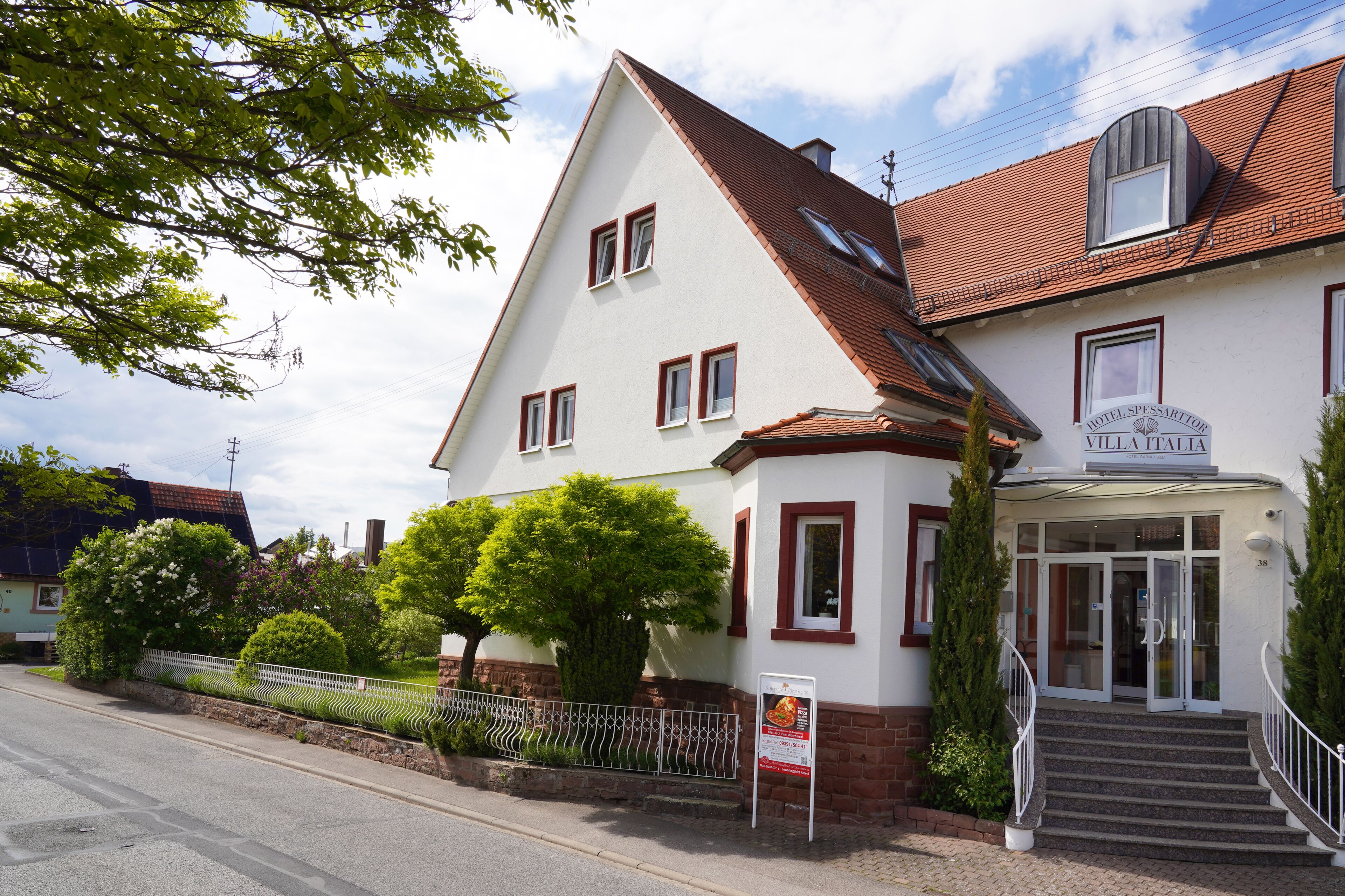 A two-story building with a red-tiled roof, a sign reading "Villa Italia," and a staircase leading to the entrance.
