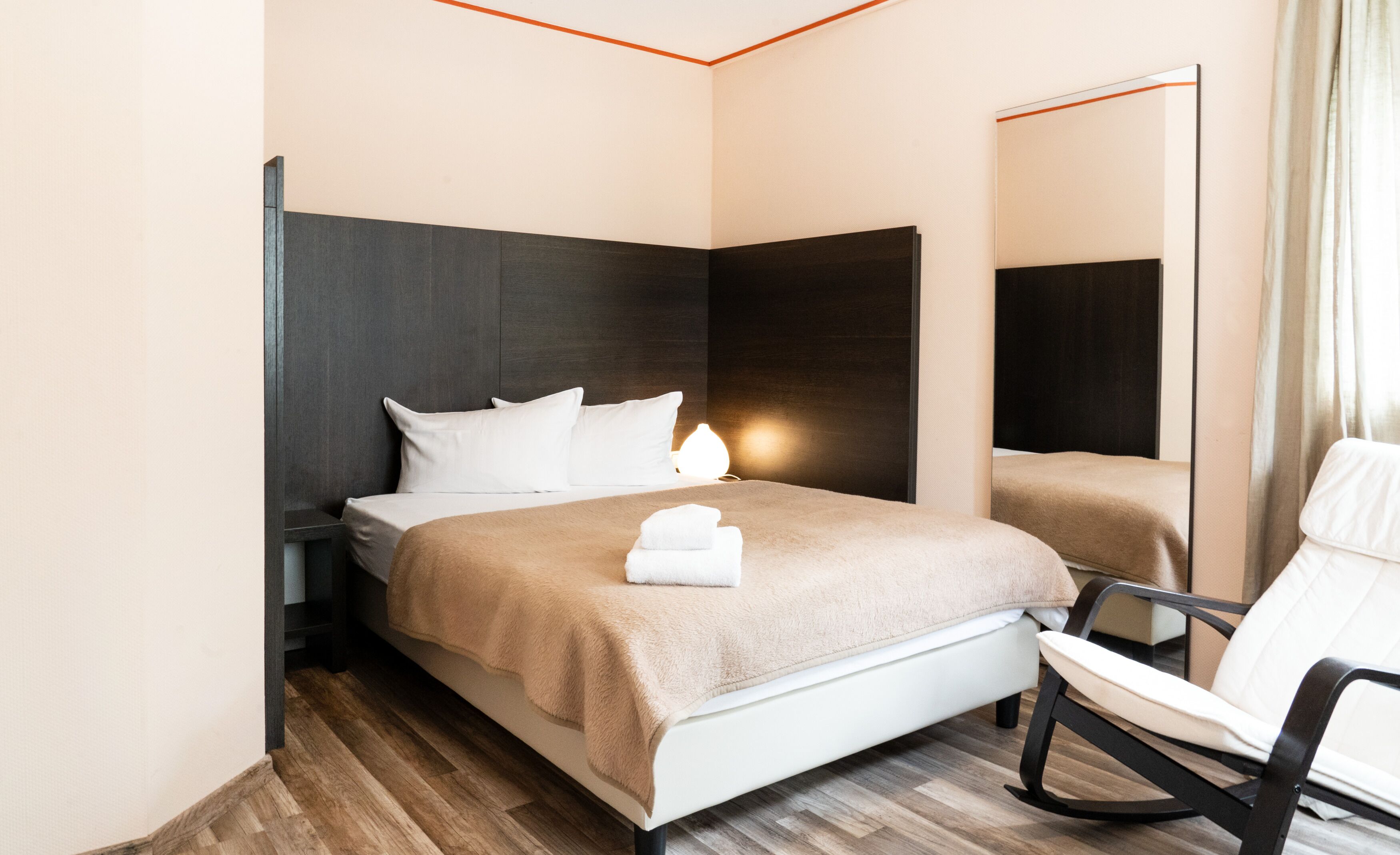 A modern hotel room with a bed, a chair, and a large mirror.